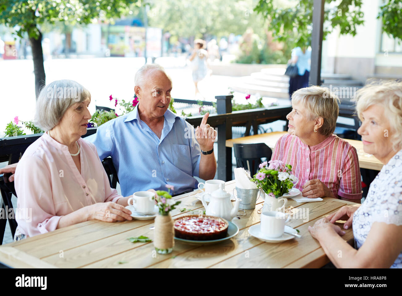 Drei ziemlich alte Frauen mit Kaffee und Käsekuchen am Café-Tisch sitzen zwar ihre männlichen Freund unterhalten sie mit Small talk Stockfoto