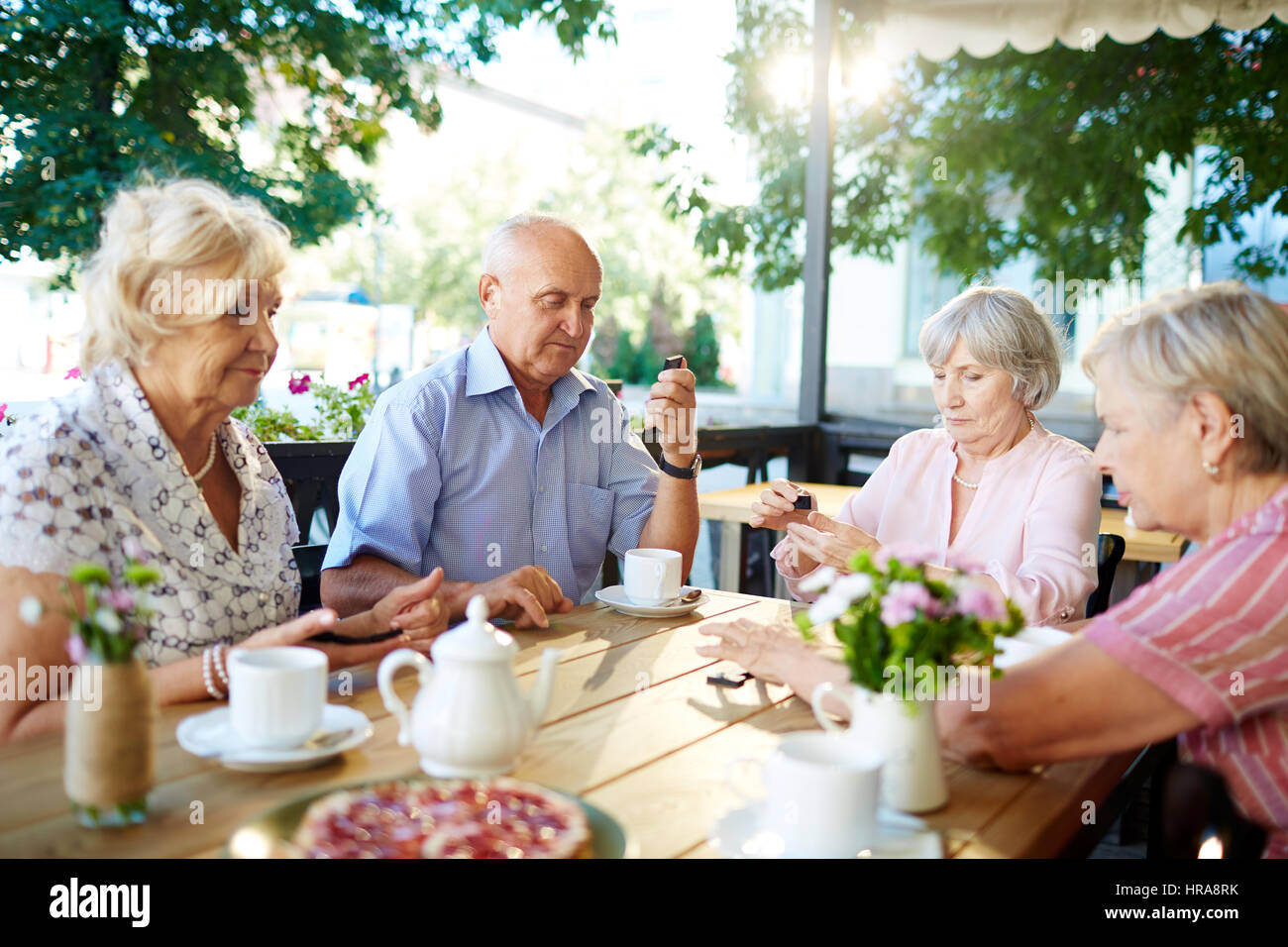 Senioren Freunde versammelten sich im Sommercafé um trinken Tee mit Gebäck und Domino spielen Stockfoto