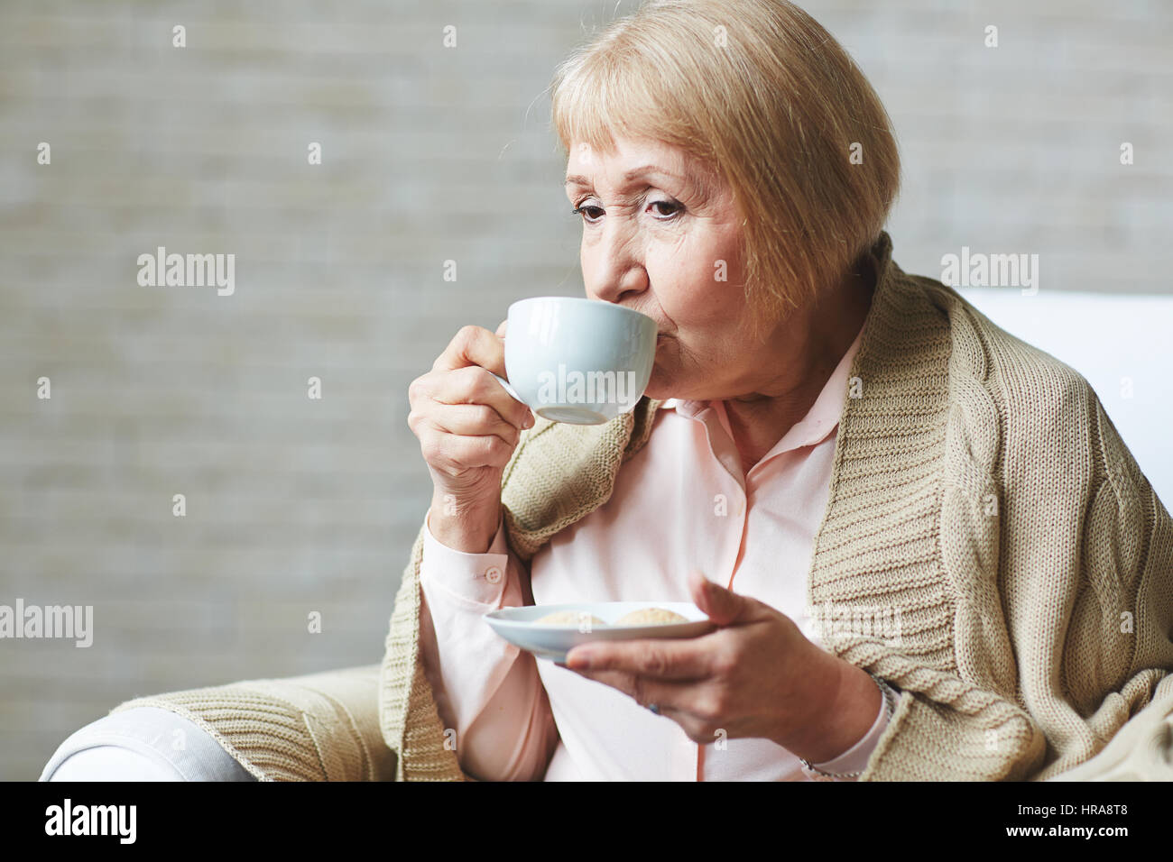 Nachdenklich Seniorin sitzt auf Sessel mit Tasse Kaffee und bedeckte Schultern mit warmen Plaid, Taille-Up portrait Stockfoto