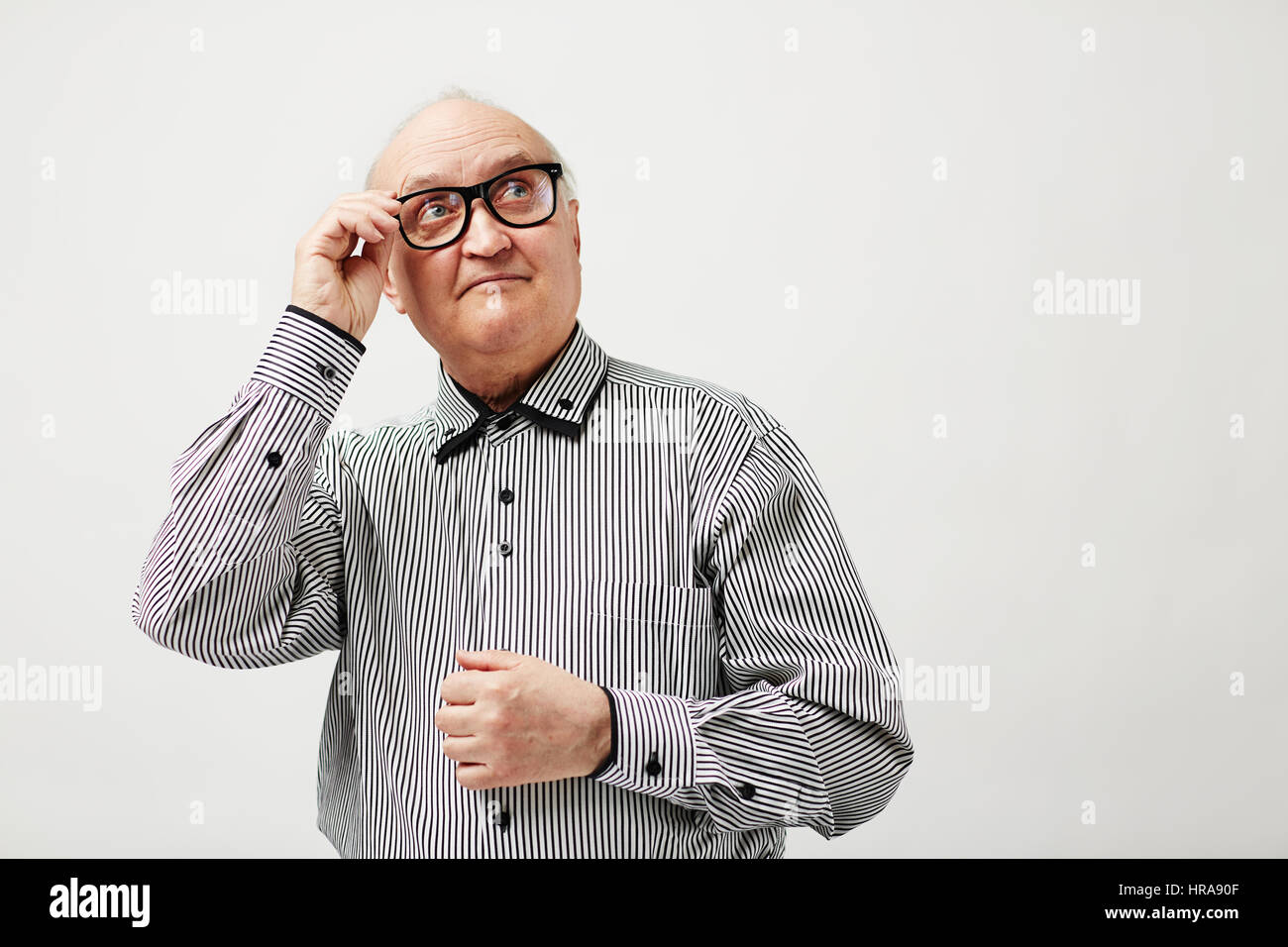 Taille-Up Portrait von eleganten alten Herrn in gestreiften Hemd Halterahmen seine Brille und blickte nachdenklich Stockfoto