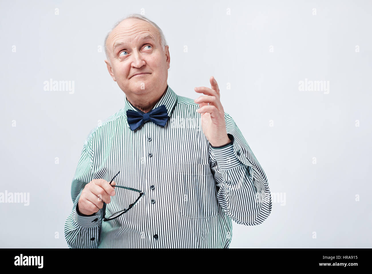 Porträt von eleganten pensionierte Mann im gestreiften Hemd mit Fliege Gläser in einer Hand halten und nach oben zeigend mit einem anderen nachdenklich Stockfoto