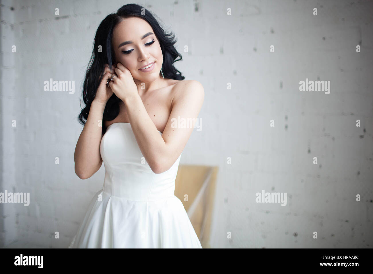 Gebräunte schöne Brünette Braut trägt Ohrringe. Modell mit langen, dunklen Haaren. Studio-Porträt auf weißem Hintergrund. Stockfoto