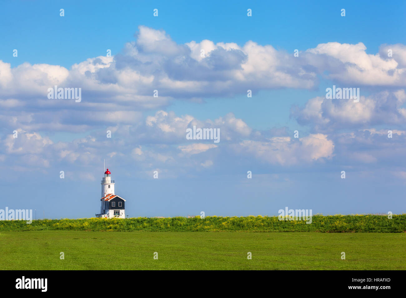 Leuchtturm auf dem Hintergrund der schönen blauen Himmel mit Wolken bei Sonnenuntergang in Niederlande. Landschaft mit bunten Wiesen, Leuchtfeuer und bewölktem Himmel Stockfoto