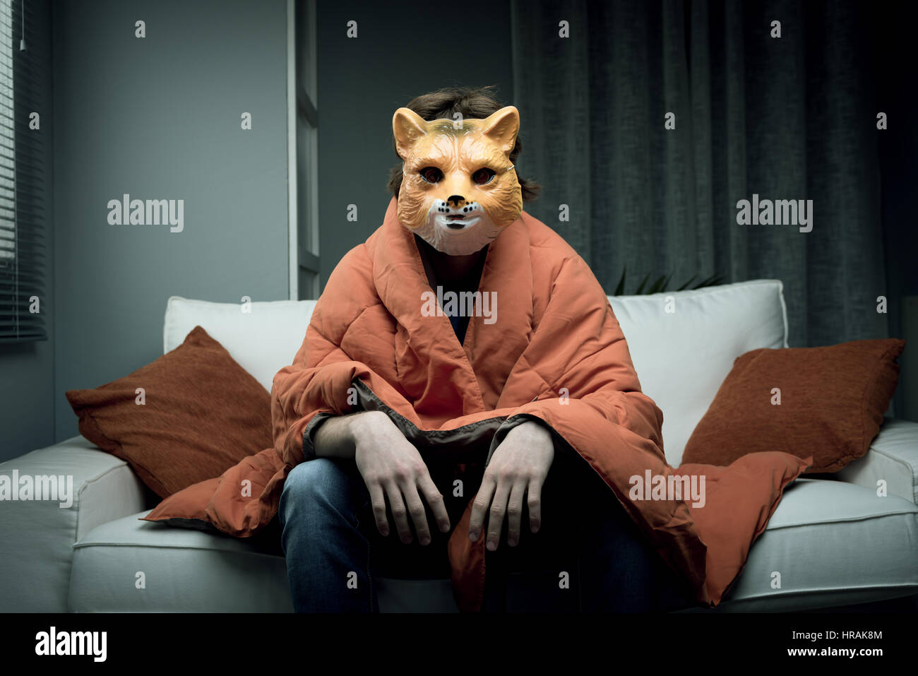 Junger Mann, der eine Fuchs Maske sitzt auf einem Sofa mit einer Decke zugedeckt. Stockfoto