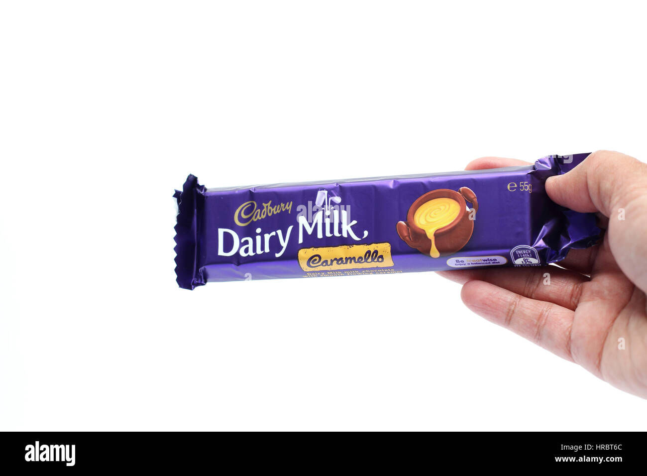 Hand hält Australien Cadbury Caramello Schokolade Bar gegen Kuhmilch Hintergrund isoliert Stockfoto