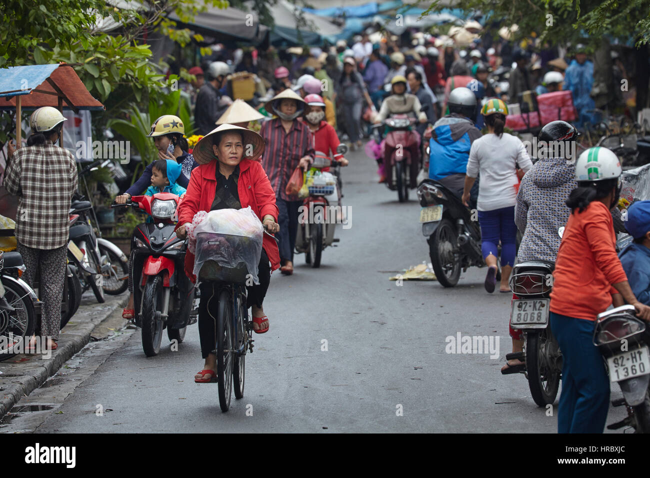 Vietnamesin mit kegelförmiger Hut auf Fahrrad auf belebten Straße Markt, Hoi an ein (UNESCO Weltkulturerbe), Vietnam Stockfoto
