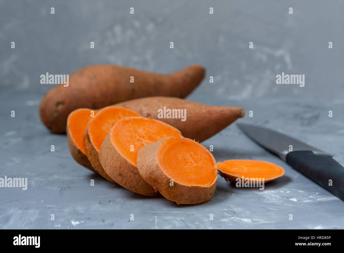 Roh in Scheiben geschnitten und ganze süße Kartoffeln auf einem dunklen Hintergrund rustikal. Stockfoto