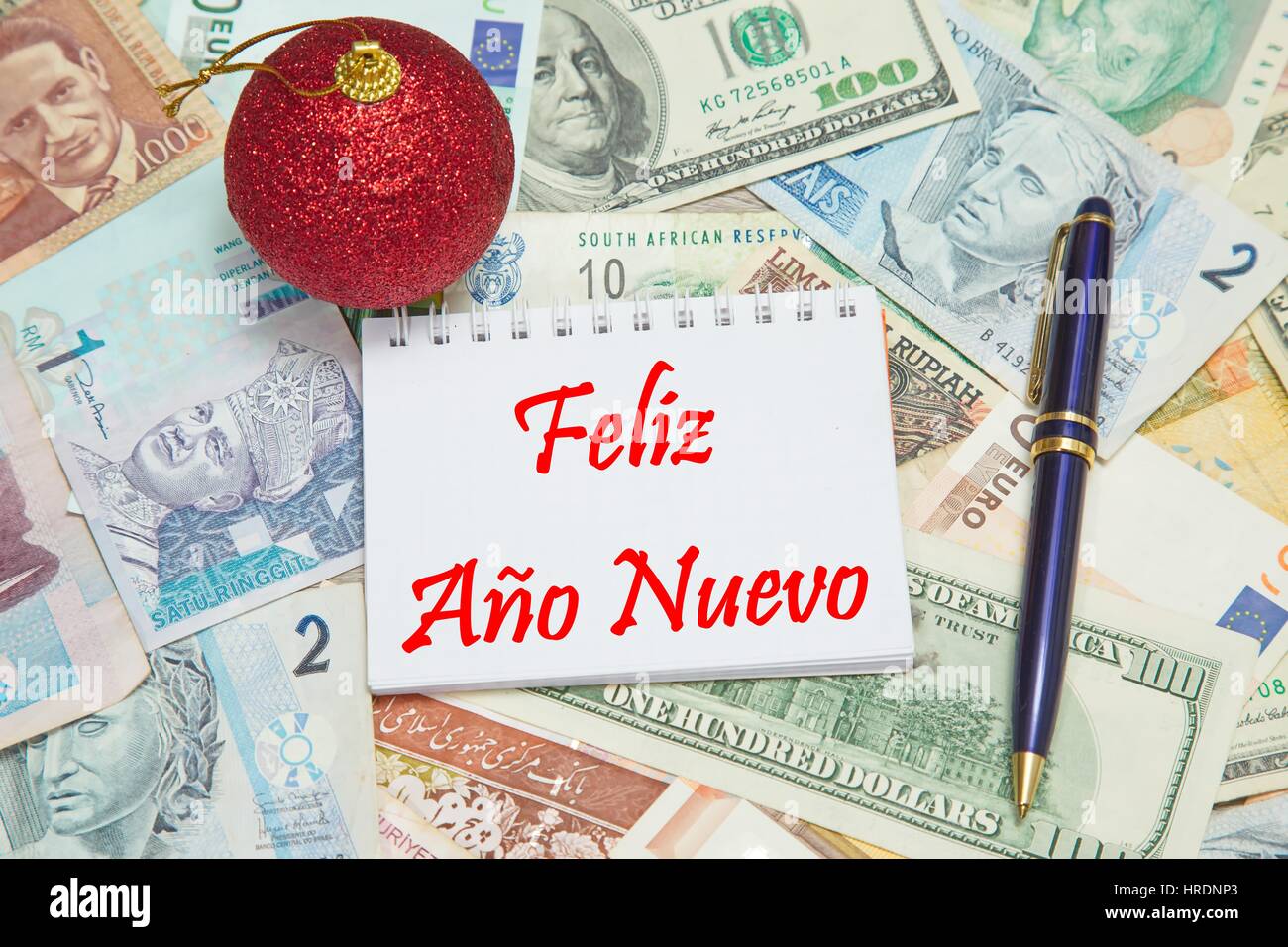 Notebook Seite mit spanischen Text 'FELIZ AÃ?O NUEVO" (FROHES NEUES JAHR), Hintergrund aus verschiedenen Währungen der Welt Stockfoto
