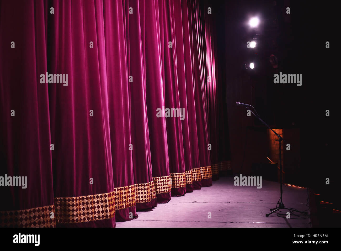 Bereit für Leistung, geschlossene Bühne mit großer dekorativer Vorhang, Mikrofon am Stand vor der es groß und Lampen und Leuchten in Ecke. Stockfoto