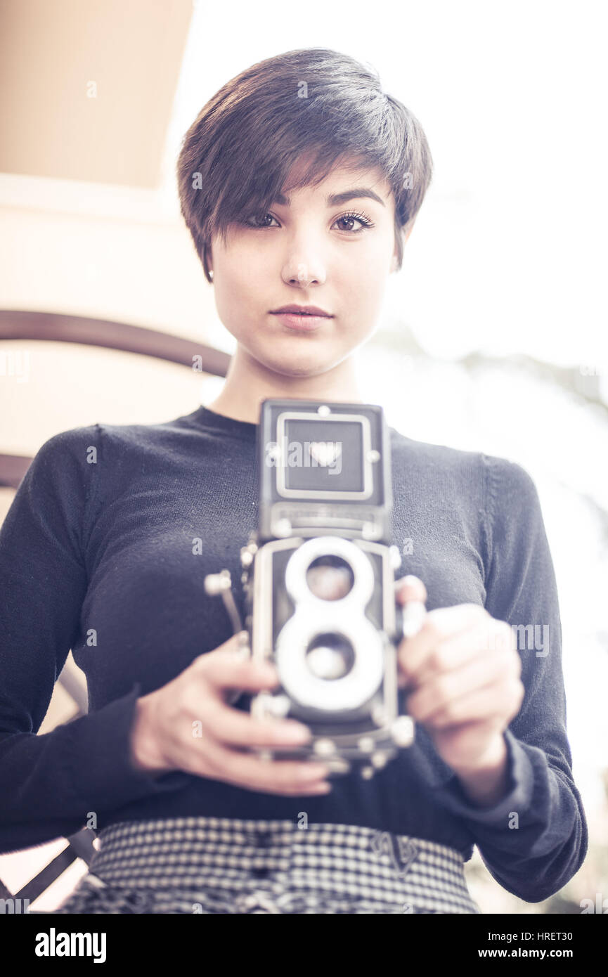 Junge hübsche Frau posiert und Blick in die Kamera mit Vintage Bi-optische Kamera zwischen den Händen Stockfoto