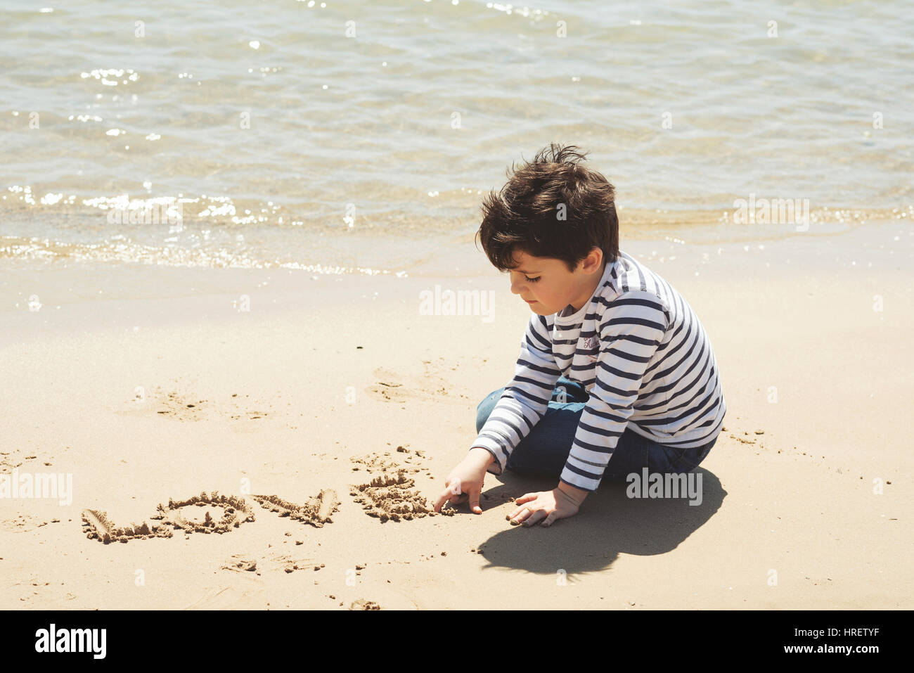 Trauriger kleiner Junge am Strand sitzen. Stockfoto