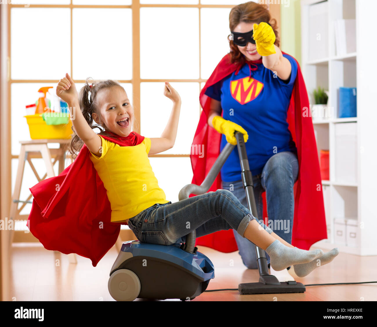 Superhelden kid Mädchen und ihre Mutter Wäsche zusammen im Wohnzimmer. Familymiddle-gealterte Frau und Kind Tochter haben Spaß beim Staubsaugen th Stockfoto