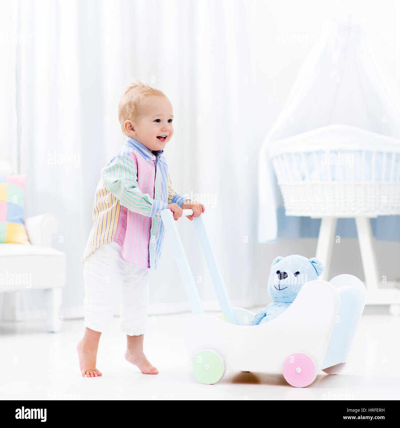 Baby Boy mit hölzernen Push Walker in weiße Schlafzimmer mit Pastell Regenbogen Farbe Spielzeug laufen lernen. Spielzeug für die ersten Schritte des Kindes zu unterstützen. Kleinkind Kind zu Fuß Stockfoto