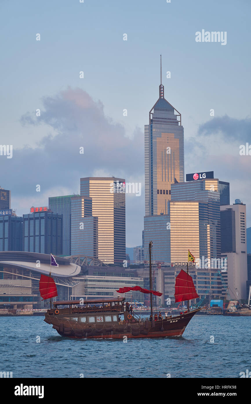 Blick von Kowloon auf das traditionelle rote Segel einer chinesischen Dschunke und über den Hafen auf die Hong Kong Skyline im Hintergrund - Hongkong, China Stockfoto