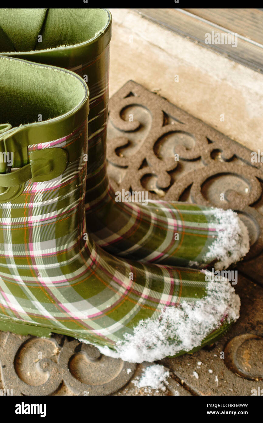 Grüne Damen Gummistiefel oder Gummistiefel, mit Schnee auf den Zehen gemustert. Ruht auf eine willkommene Matte. Stockfoto