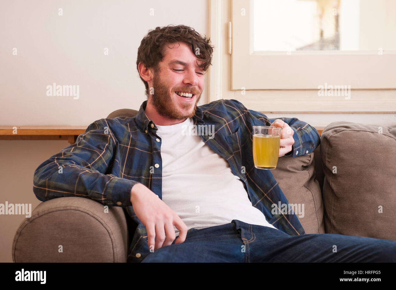 Junger Mann in seinem Wohnzimmer mit einem karierten Hemd und ein Buch Stockfoto