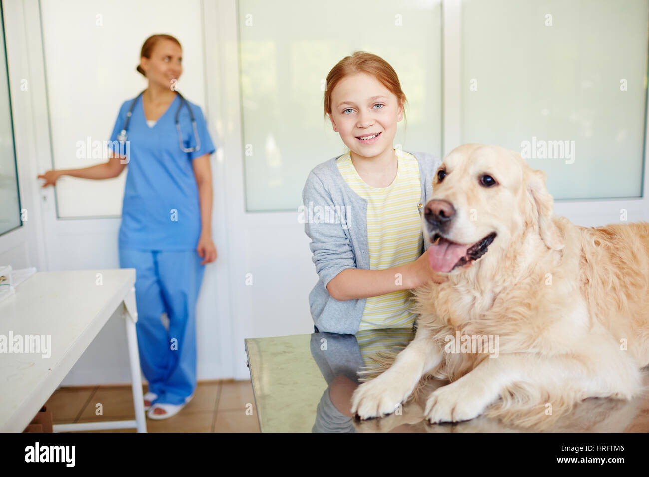Kleine rothaarige Besitzer stehen neben ihrem Hund ruht auf den Untersuchungstisch nach Checkup und lächelt in die Kamera hell Stockfoto