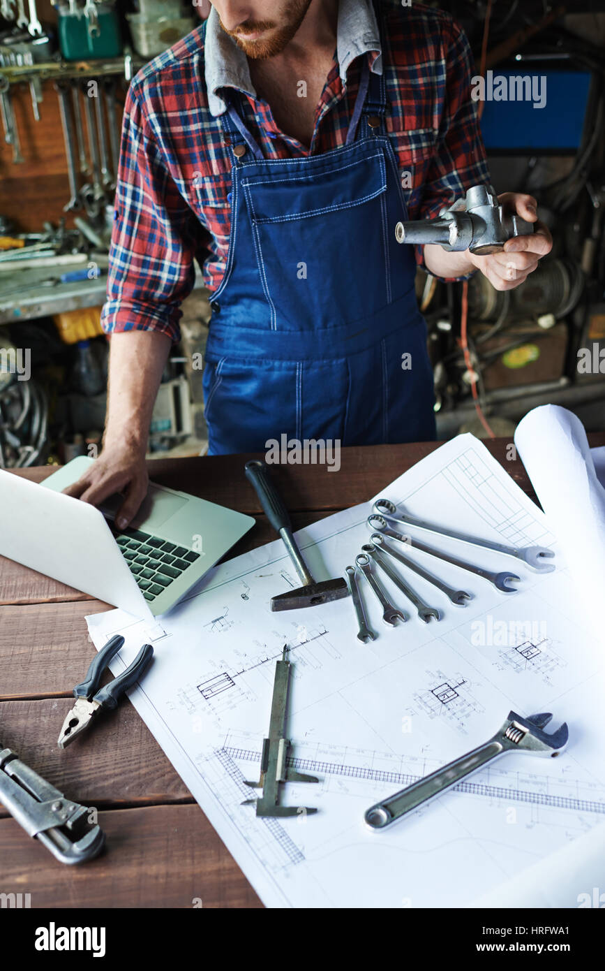 Unkenntlich moderne Mechaniker in Garage arbeiten an groben Holztisch mit sortierten Mechanik Werkzeuge, Schraubenschlüssel, hammer und Zange auf angelegt mit Stockfoto