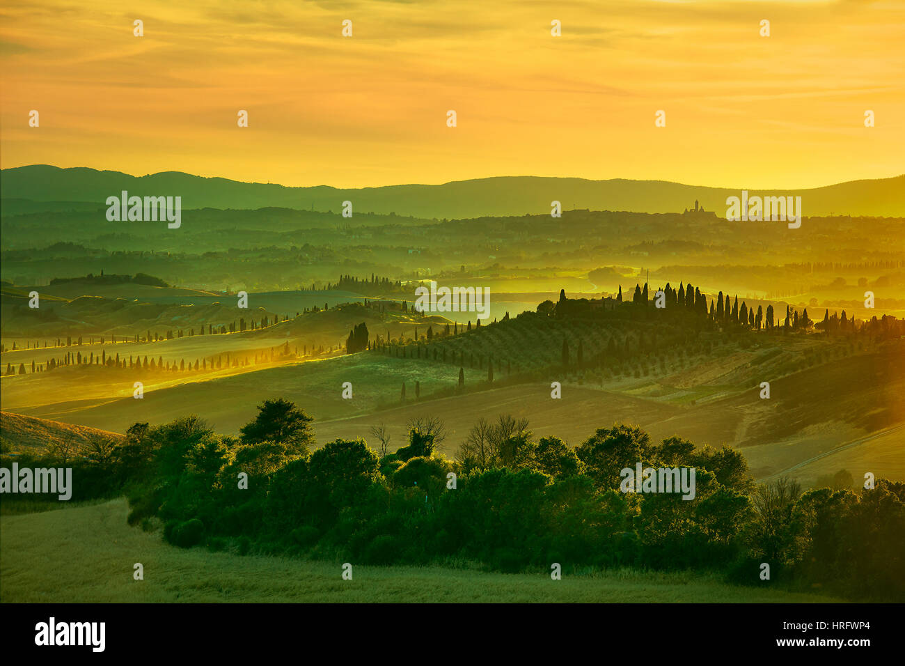 Toskana, sanfte Hügel im Sonnenuntergang. Landschaft der Crete Senesi. Grüne Felder, ein Bauernhof mit Zypressen und Siena Stadt auf Hintergrund. Italien Stockfoto