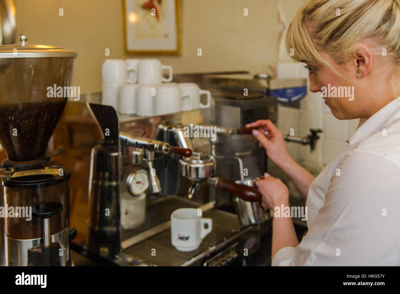 Weibliche barista verwendet eine professionelle Kaffeemaschine eine Latte zu machen. Stockfoto