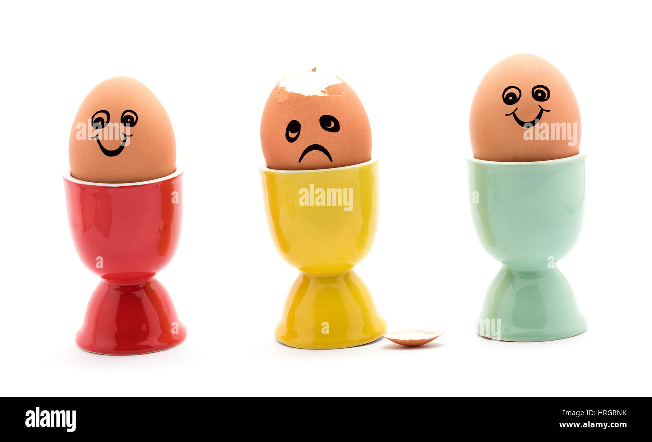 Ein trauriges gekochtes Ei in eine gelbe Eierbecher zwei glückliche Eier rot und grün Eierbecher. Stockfoto
