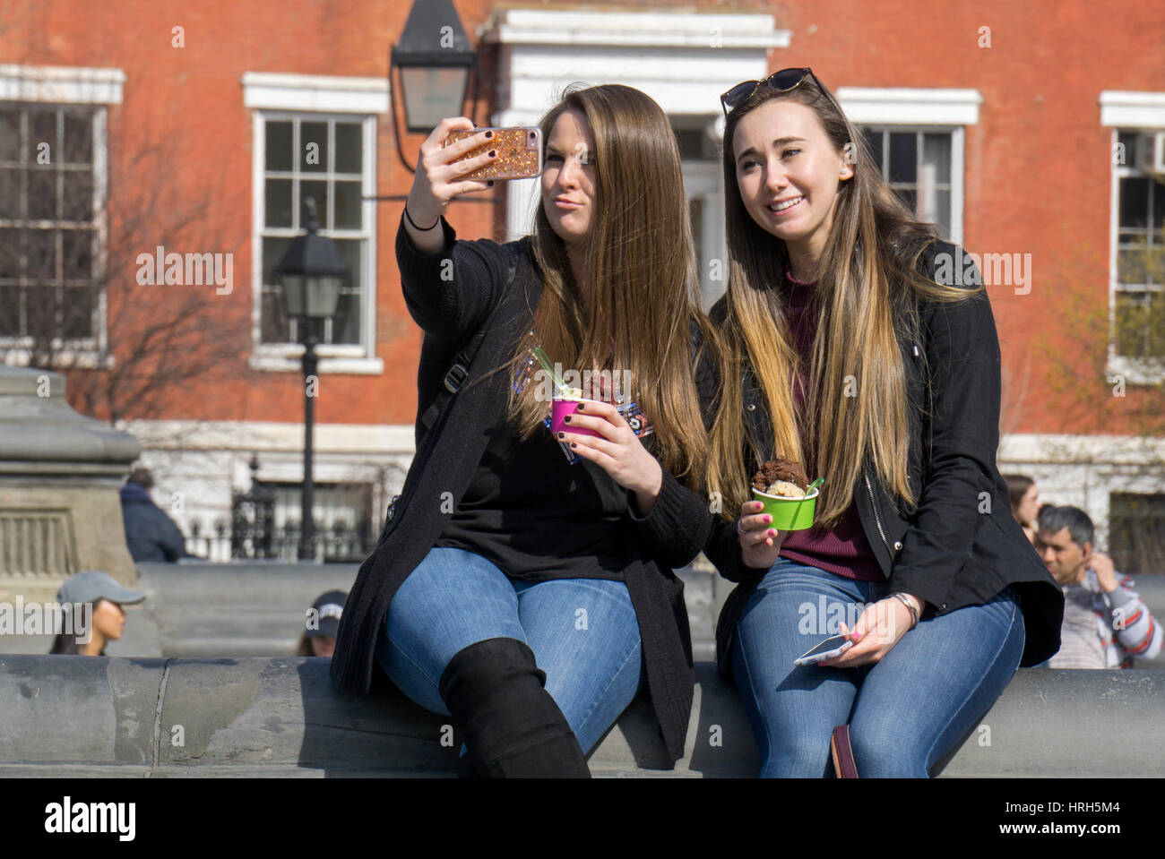 Zwei attraktive junge Damen mit Eis nehmen ein Selbstporträt im Washington Square Park in Greenwich Village, Manhattan, New York City. Stockfoto