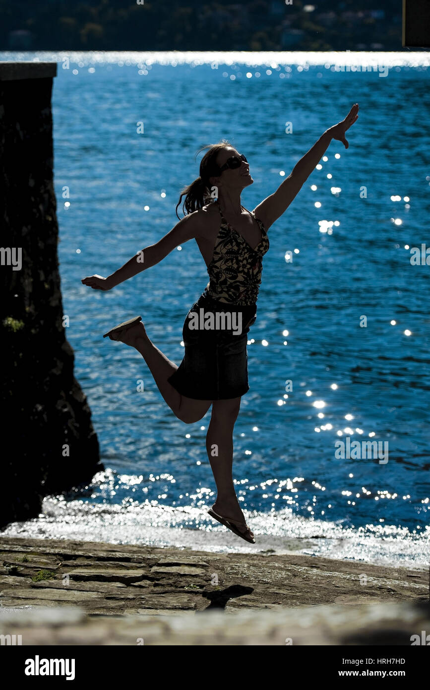 Model freigegeben, Silhouette Einer Springenden Frau bin Seeufer, Italienisch - Silhouette einer springenden Frau am Meer Stockfoto