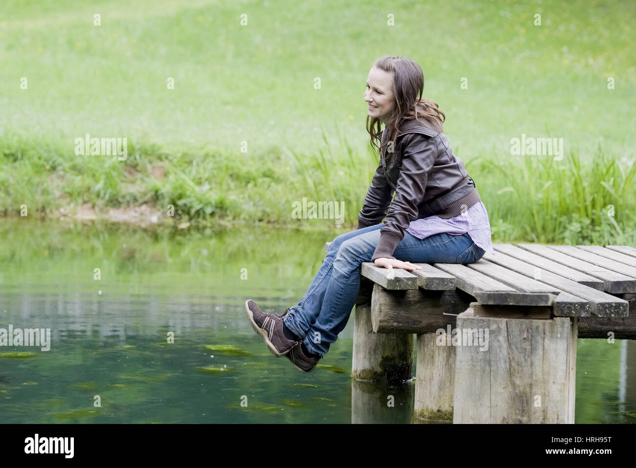 Frau Sitzt Wohnhauses Auf Steg 'm Teich - Frau entspannen Sie sich auf eine Teich-Brücke Stockfoto