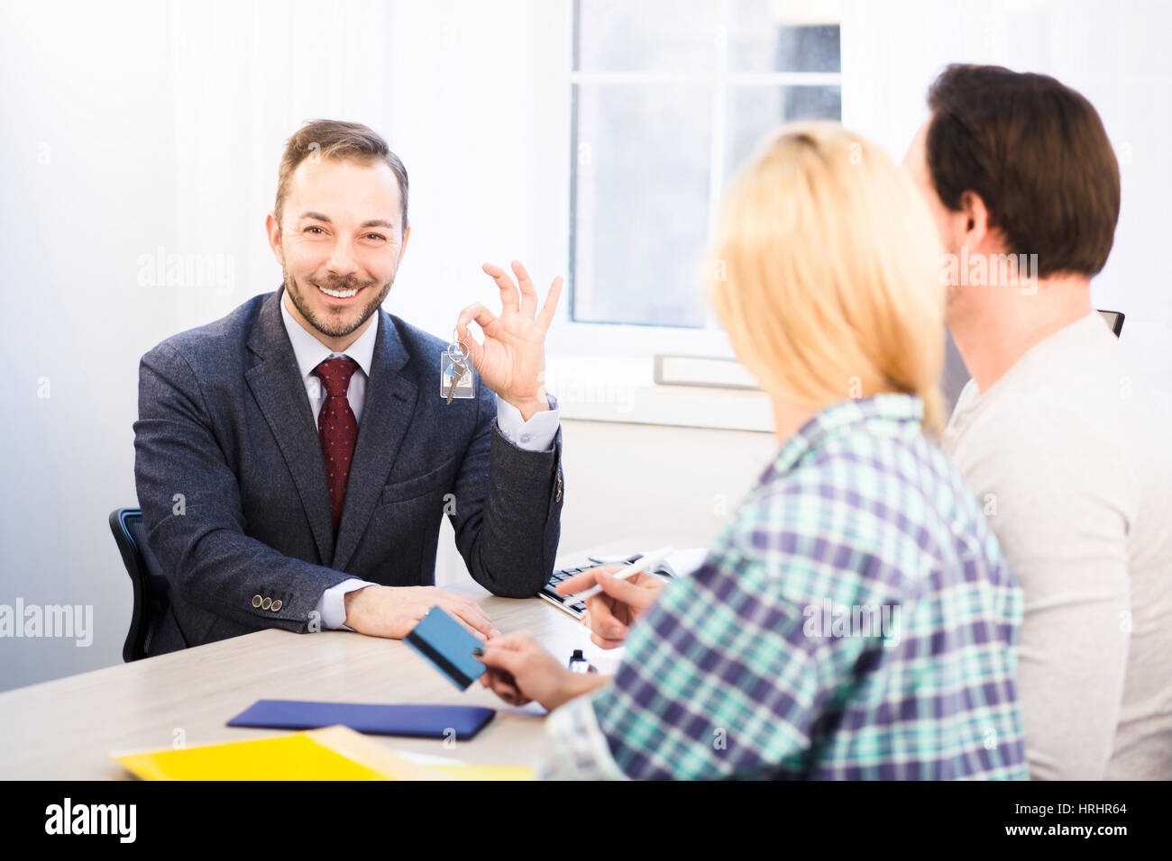 Getönten Vertriebsleiter junges Paar Schlüssel geben. Glücklich Verkaufsleiter zeigt Schlüssel zur Kamera und bietet entsprechende Vereinbarungen oder Verträge für Testdauer Stockfoto