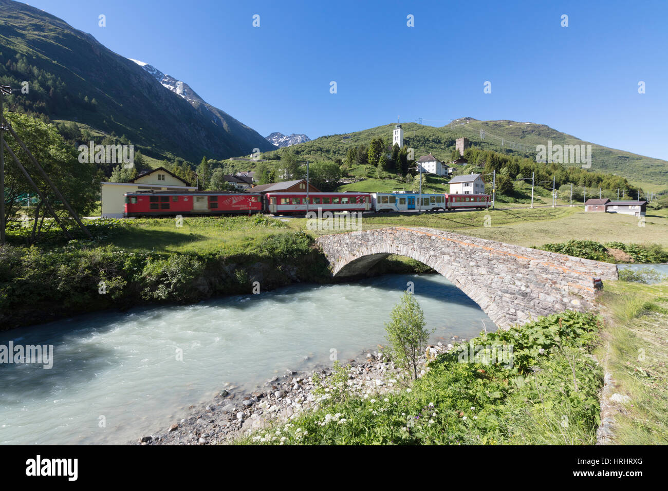 Typische rote Schweizer Schulen an Hospental Viadukt umgeben von Creek und grüne Wiesen, Andermatt, Kanton Uri, Schweiz Stockfoto