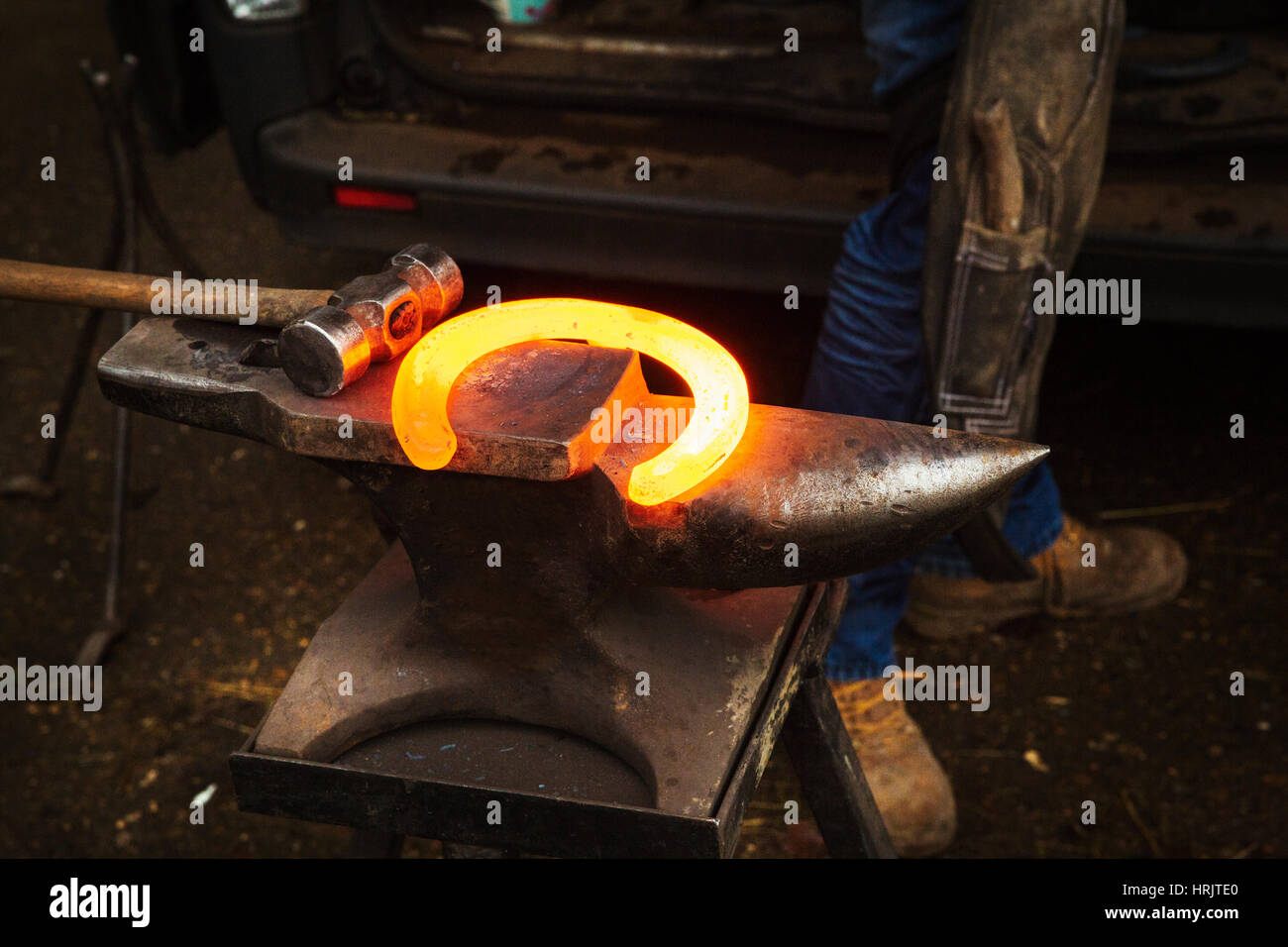 Hammer und Amboss und ein rotes Glühen erhitzt Metall Hufeisen. Stockfoto