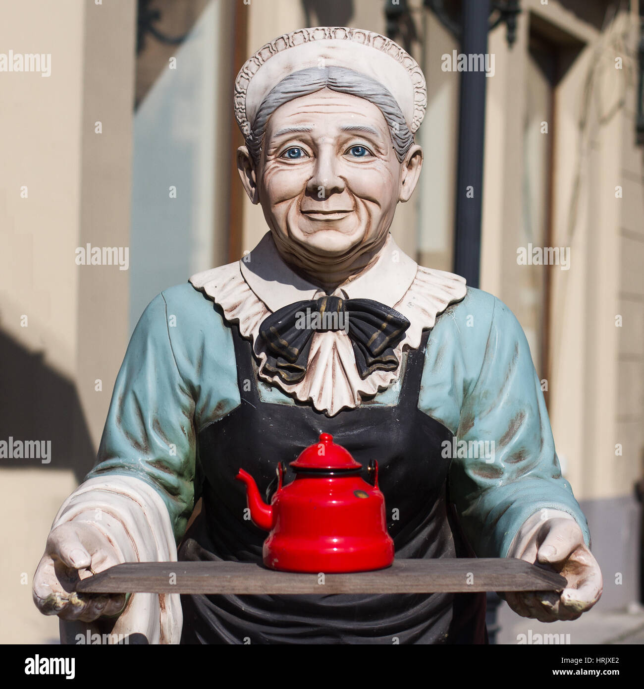 Vorderansicht der alten Frau farbige Statue hält einen Vintage roter Tee Wasserkocher auf einem Holzbrett Stockfoto