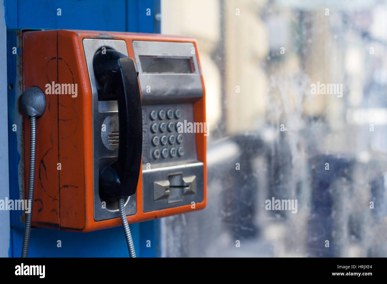 Vertikale Seitenansicht des beschädigten orange öffentliches Telefon mit schmutzigen Fenster mit selektiven Fokus Stockfoto