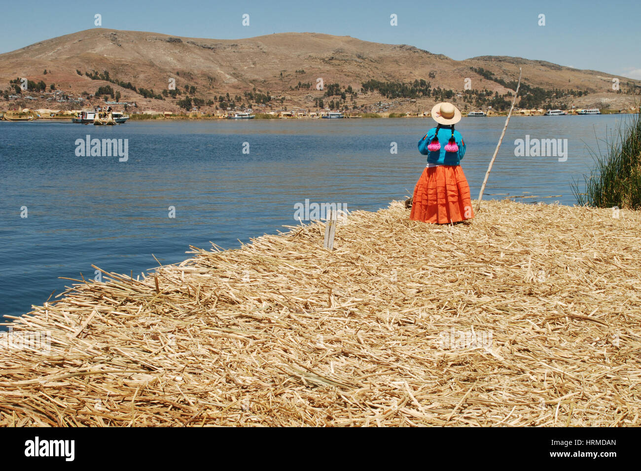 Eine Frau, gekleidet in traditionellen peruanischen Kleidung schaut zum Titicaca-See und die Stadt Puno aus den Uros Inseln (oder schwimmenden Inseln) in Peru Stockfoto