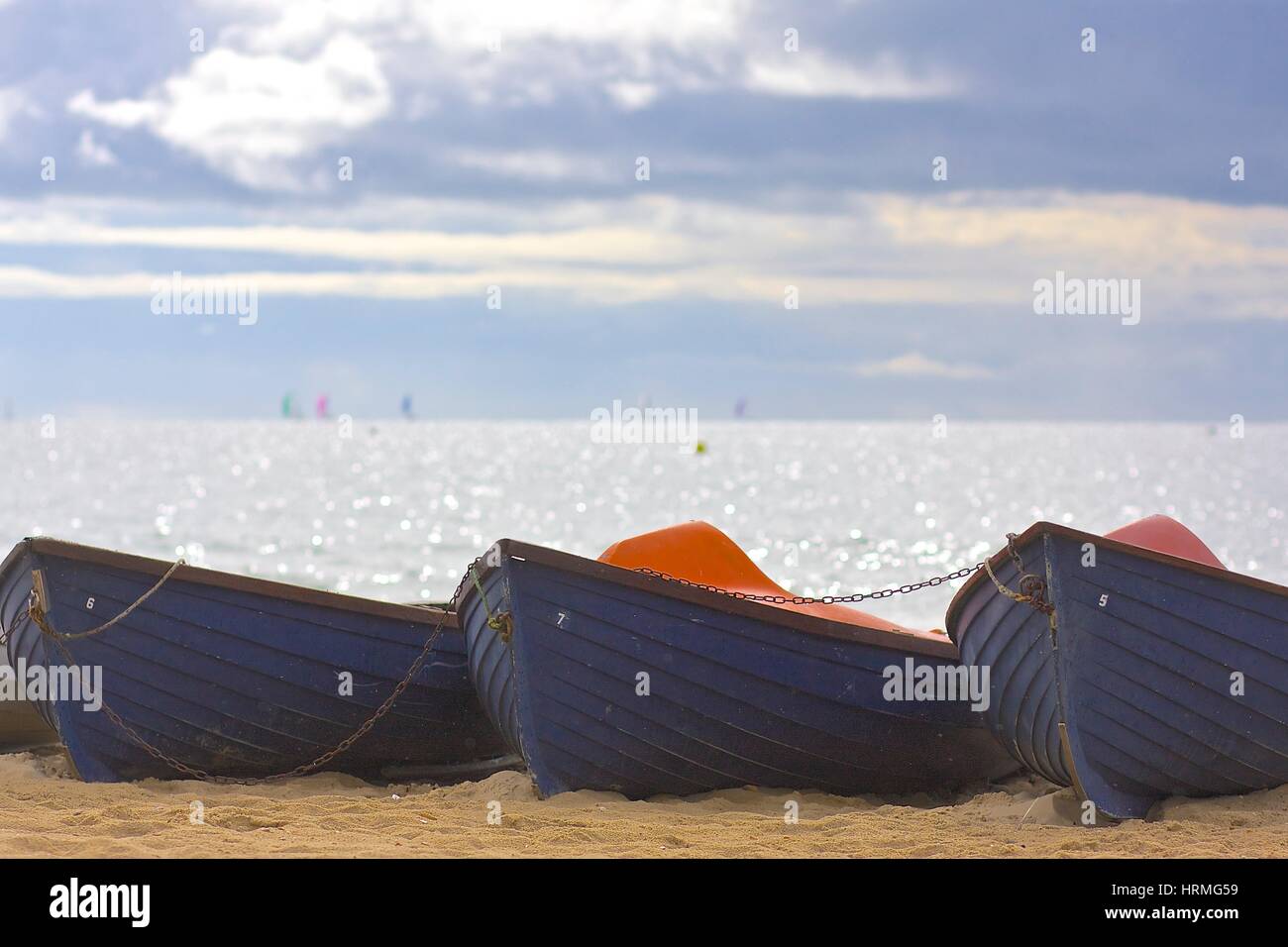 Boote an einem Sandstrand mit glitzernden Meer und Segelboote am Horizont Stockfoto