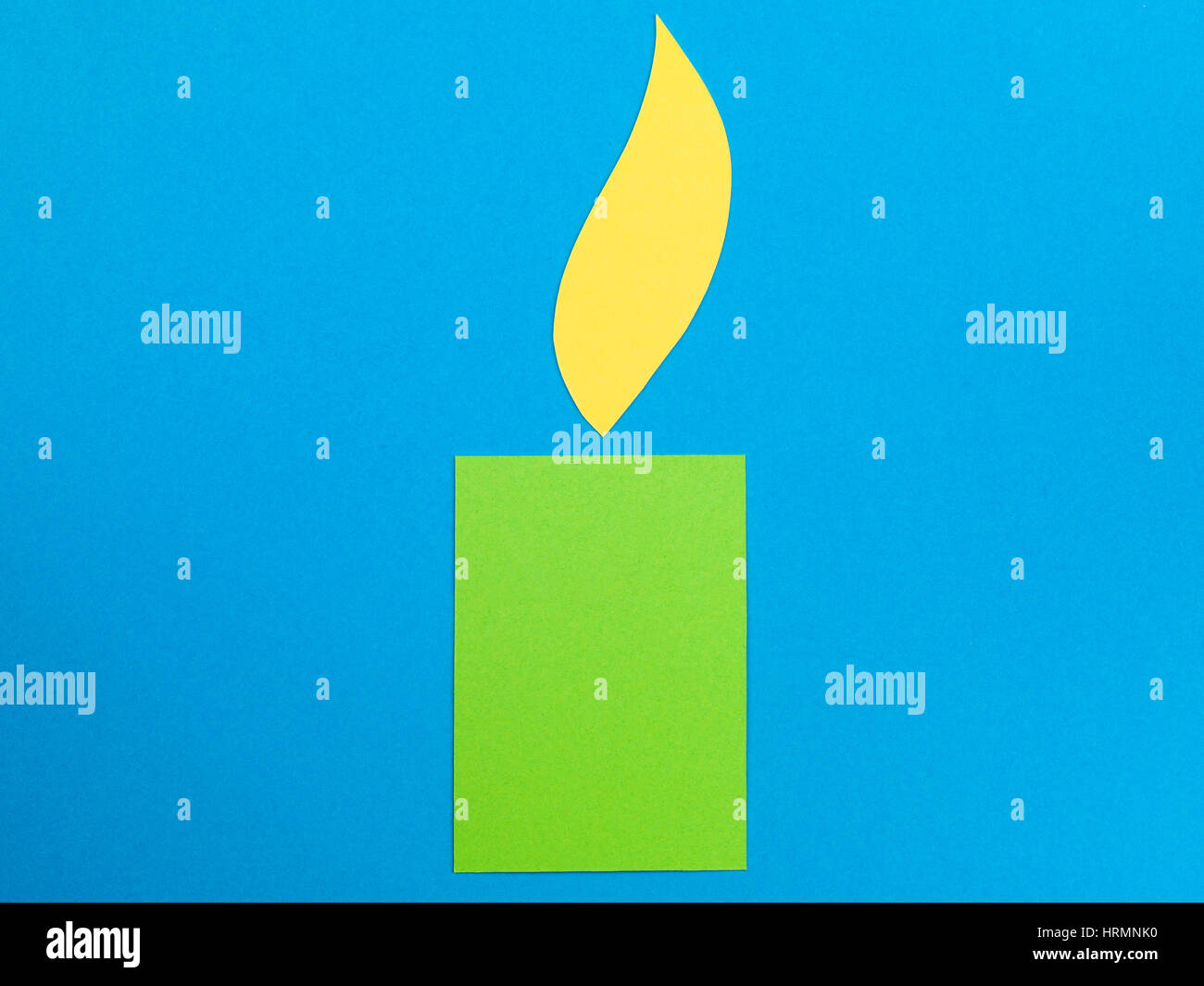 Beispiel für eine grüne Kerze mit einer gelben Flamme auf blauem Grund Stockfoto