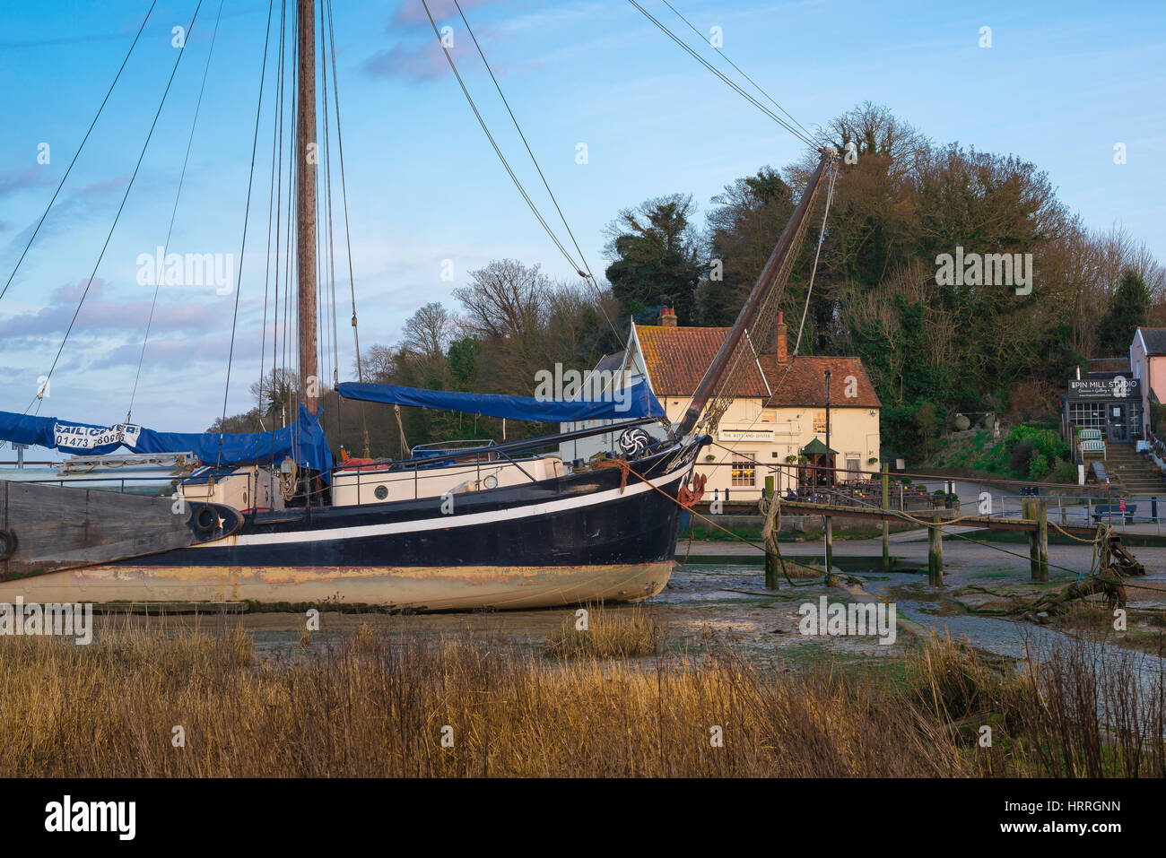 Suffolk Landschaft sitzt ein Vintage Segelboot in der River Orwell bei Ebbe mit der Dorfkneipe im Hintergrund, Pin Mill, England, UK Stockfoto
