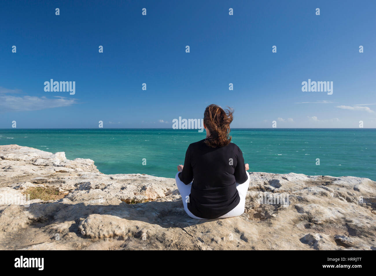 FRAU, MEDITIEREN AUF KLIPPE IN YOGA POSITION FACING MEER CABO ROJO PUERTO RICO Stockfoto