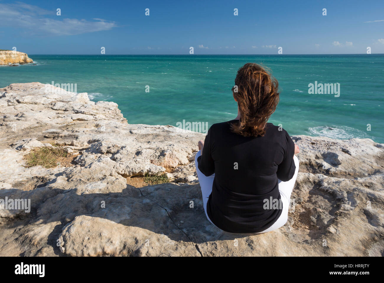 FRAU, MEDITIEREN AUF KLIPPE IN YOGA POSITION FACING MEER CABO ROJO PUERTO RICO Stockfoto