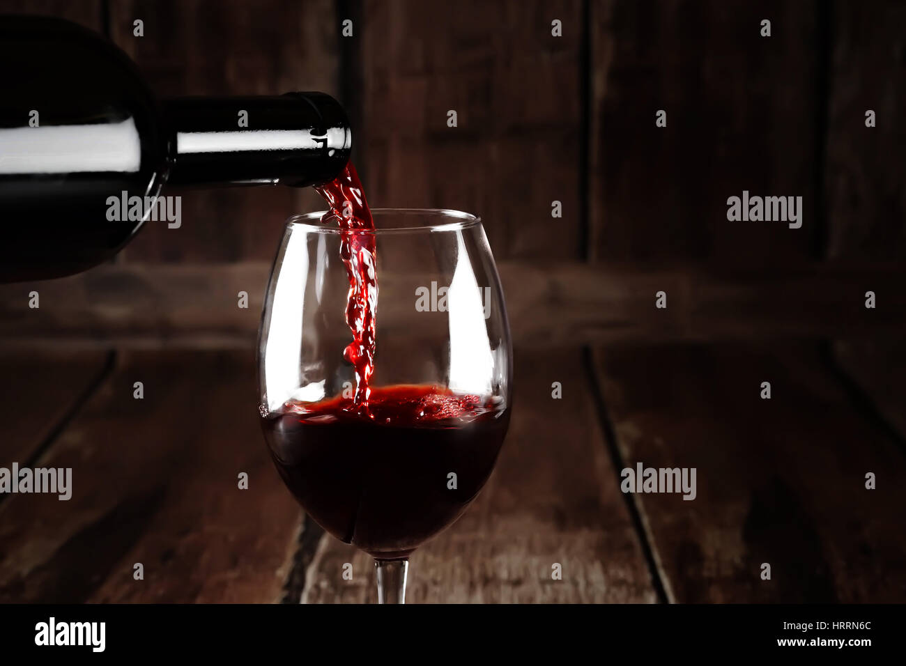 Wein im Glas auf braunem Hintergrund aus Holz. Rot Wein gießen aus Flasche. Nahaufnahme von roten Wein Splash. Hintergrund mit Rotwein ablöschen. Stockfoto