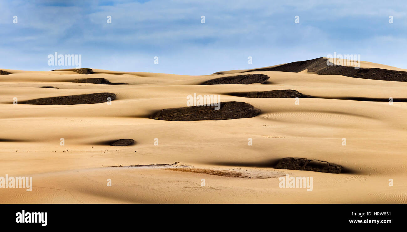 Dunkle Flecken der Schritt Seiten der Sanddünen in endlosen Sand der Wüste unter blassen blauen Himmel. Leblose Sand Massen in der Nähe von Stockton Beach of New South Wales, Australien. Stockfoto
