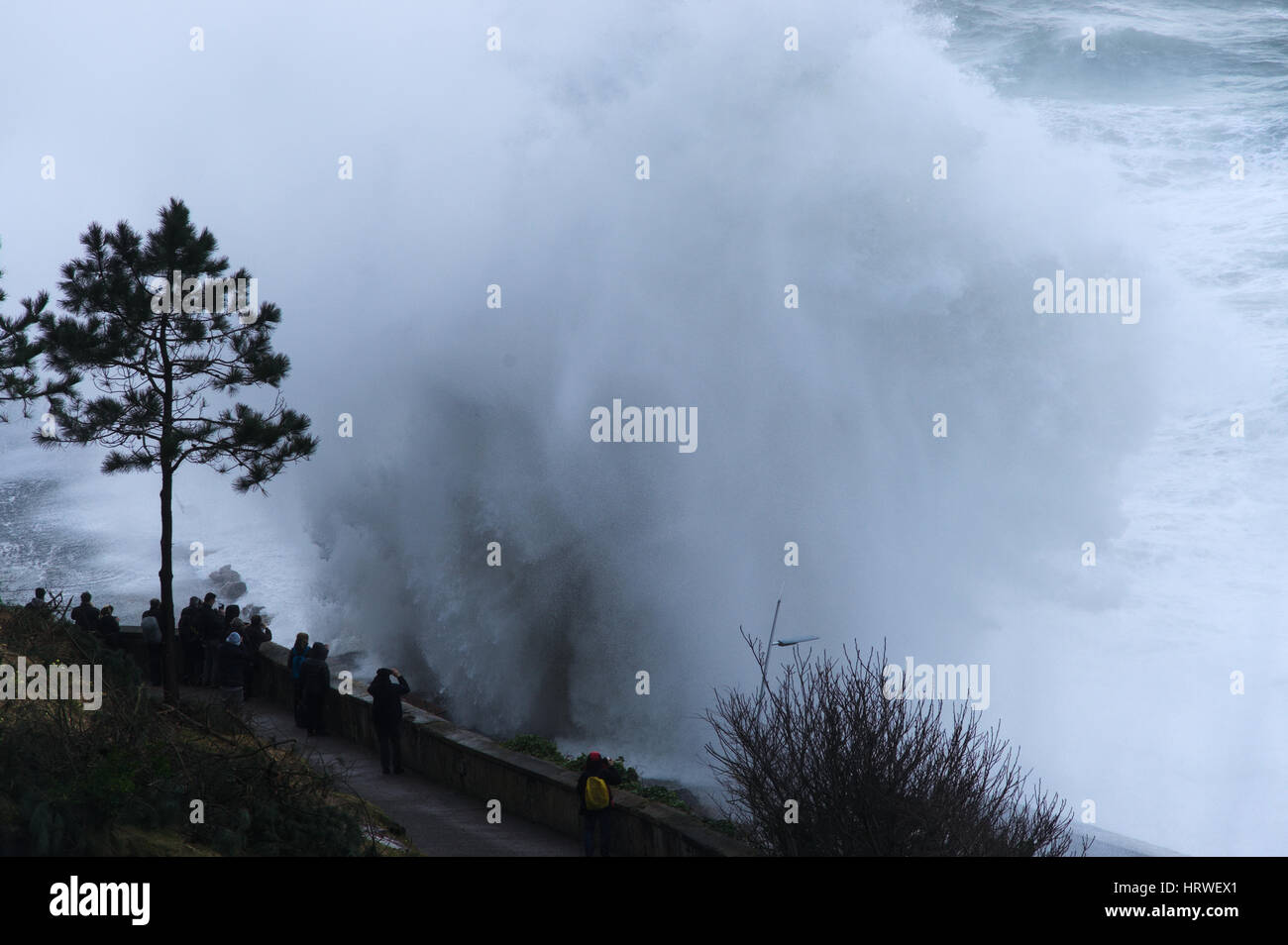 Einige Leute genießen Sie die Wellen brechen sich an der Küste in San Sebastian, Spanien. Stockfoto