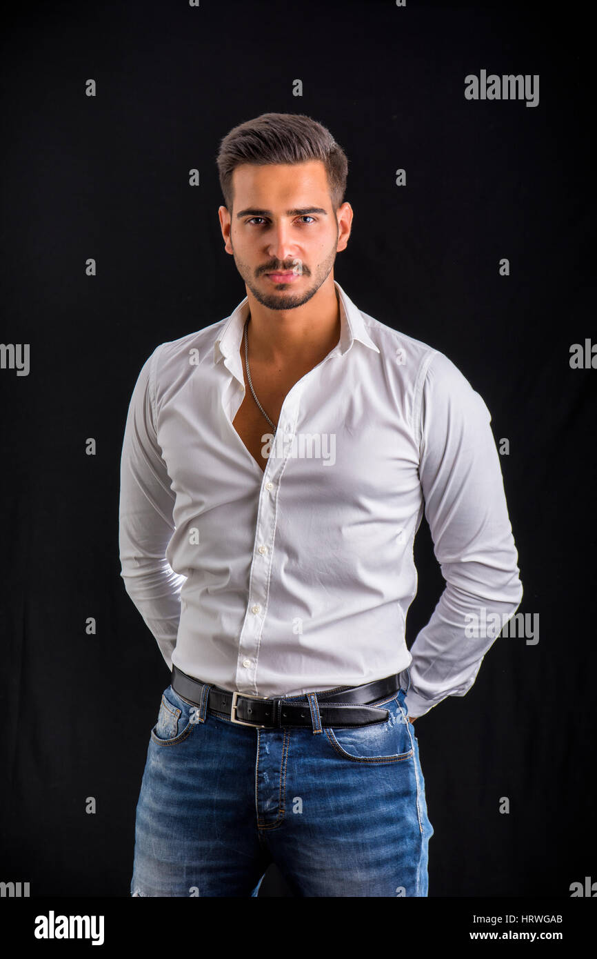 Junger Geschäftsmann zuversichtlich posieren vor der Kamera, trägt weißes Hemd zu öffnen, am Hals, auf dunklem Hintergrund Stockfoto