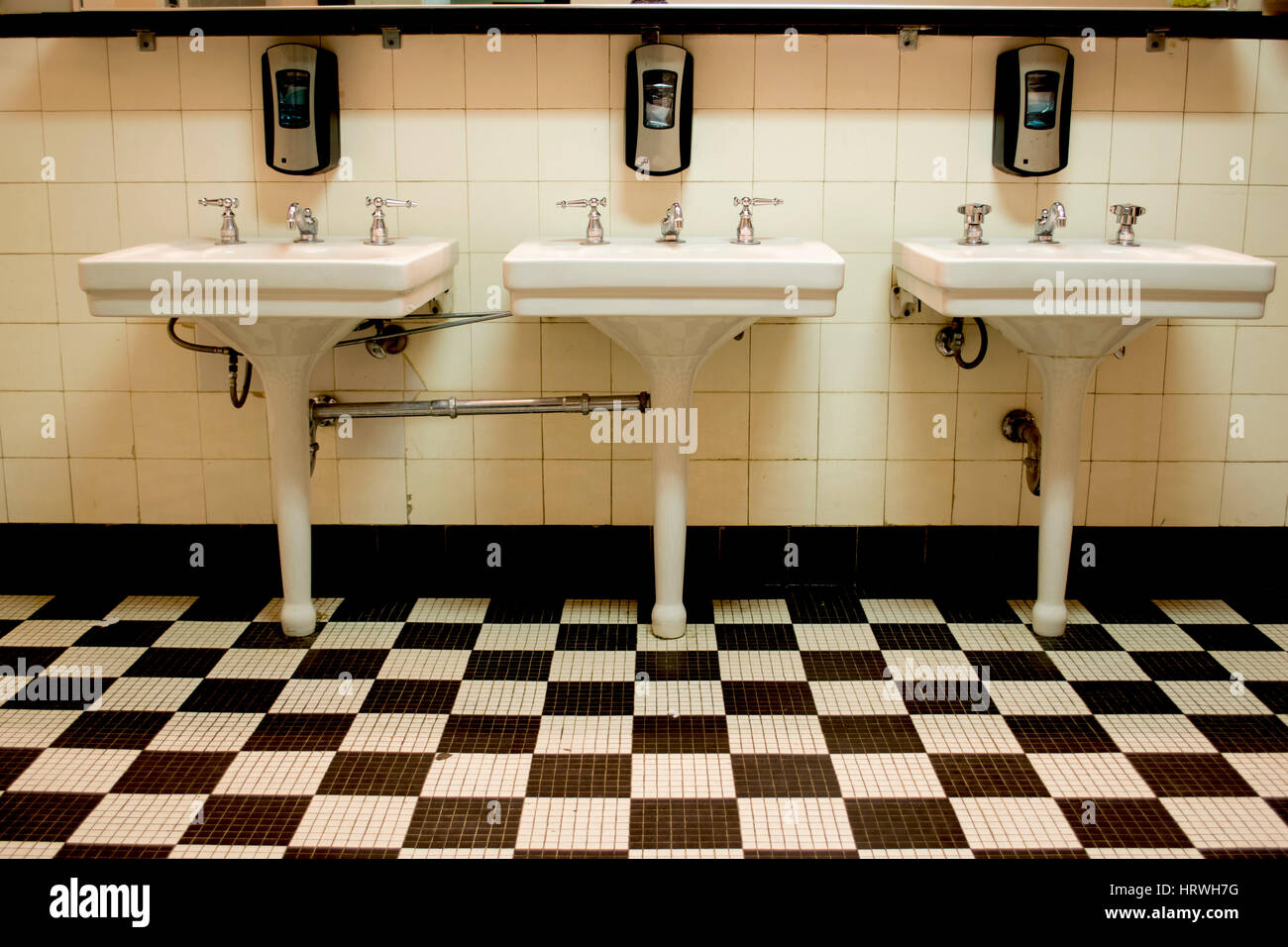 Drei weiße Porzellan Waschbecken in einem alten Art-Deco-öffentliche Badezimmer mit einem schwarz-weiß karierten Fliesenboden. Stockfoto