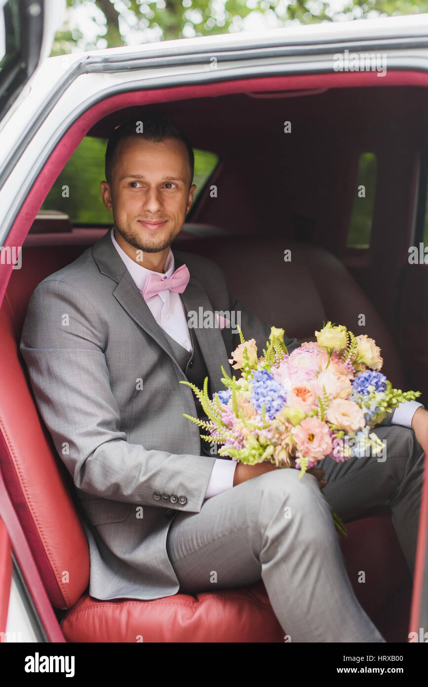 Schöne stilvolle Bräutigam mit Blumenstrauß in das Hochzeitsauto. Ein Mann in einem Anzug mit einer Fliege. Blick zur Seite. Stockfoto