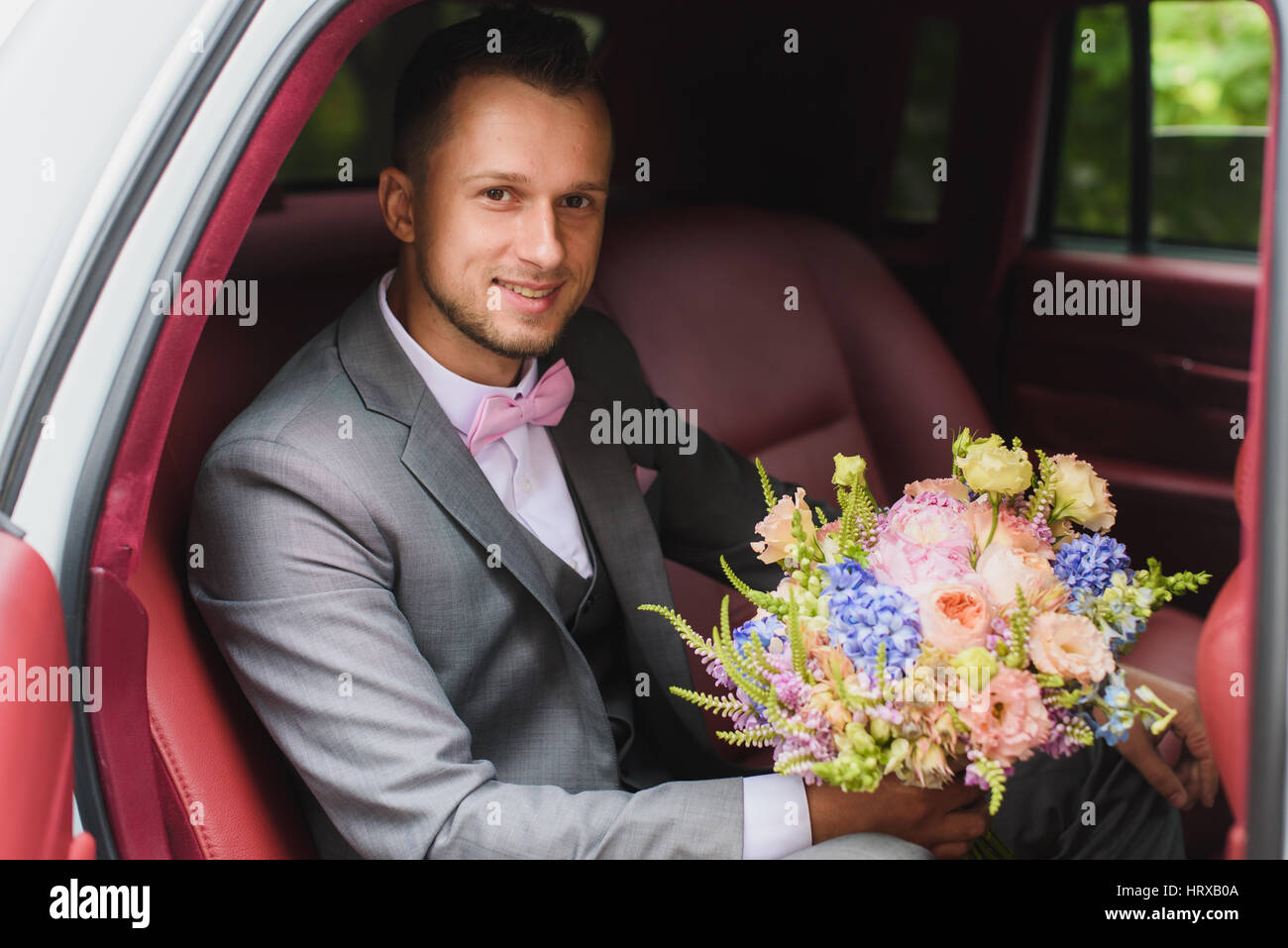 Schöne stilvolle Bräutigam mit Blumenstrauß in das Hochzeitsauto. Ein Mann in einem Anzug mit einer Fliege. Stockfoto