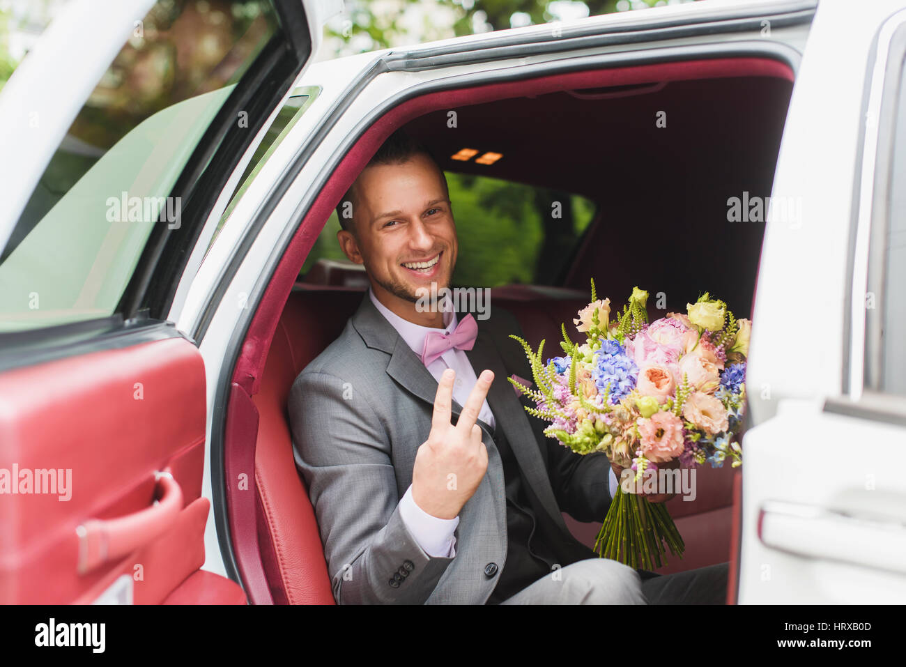 Schöne stilvolle Bräutigam mit Blumenstrauß in das Hochzeitsauto. Ein Mann in einem Anzug mit einer Fliege. Stockfoto