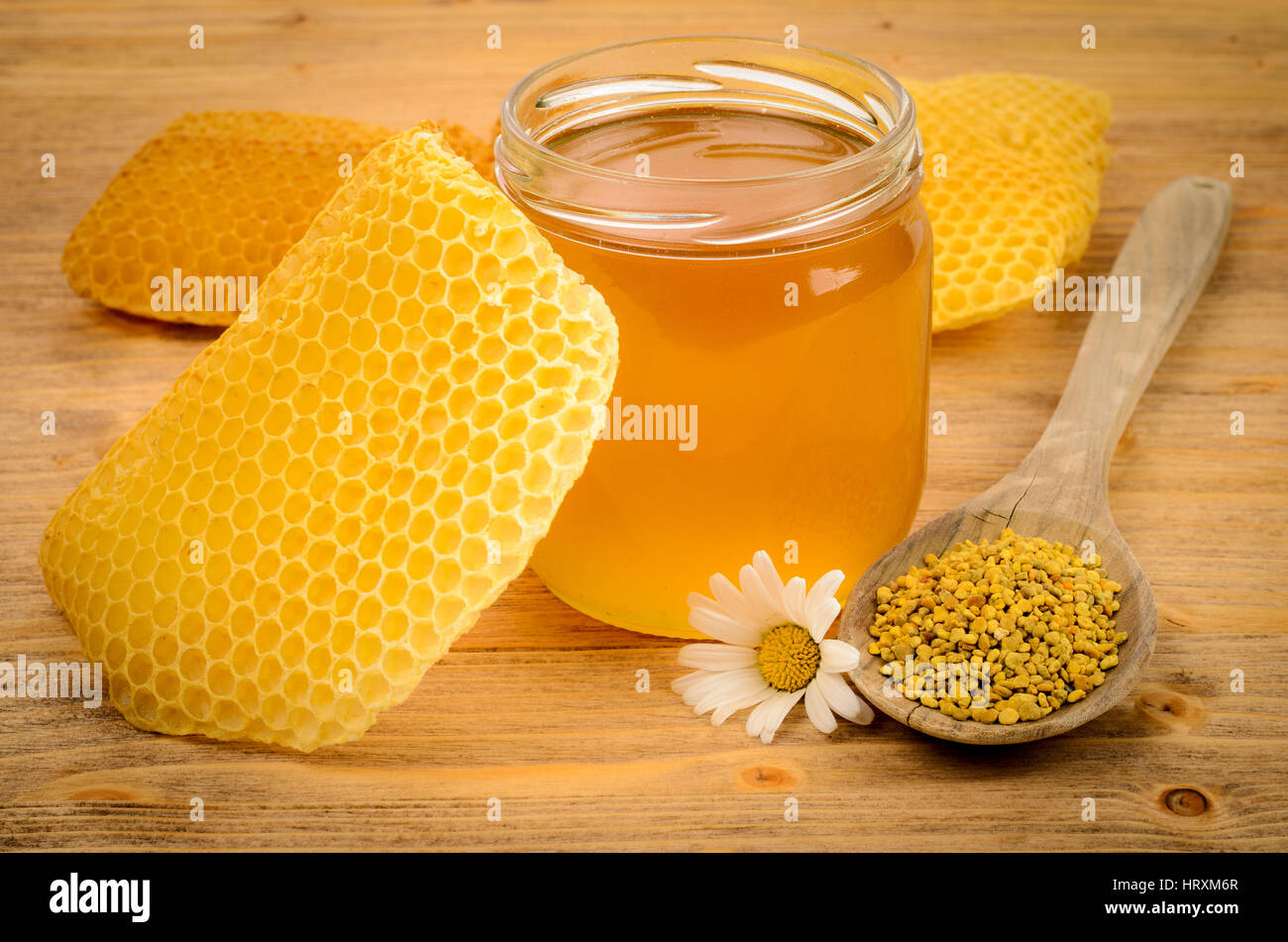 Glas voller Honig mit Waben und Holzlöffel mit Pollen auf Holztisch Stockfoto