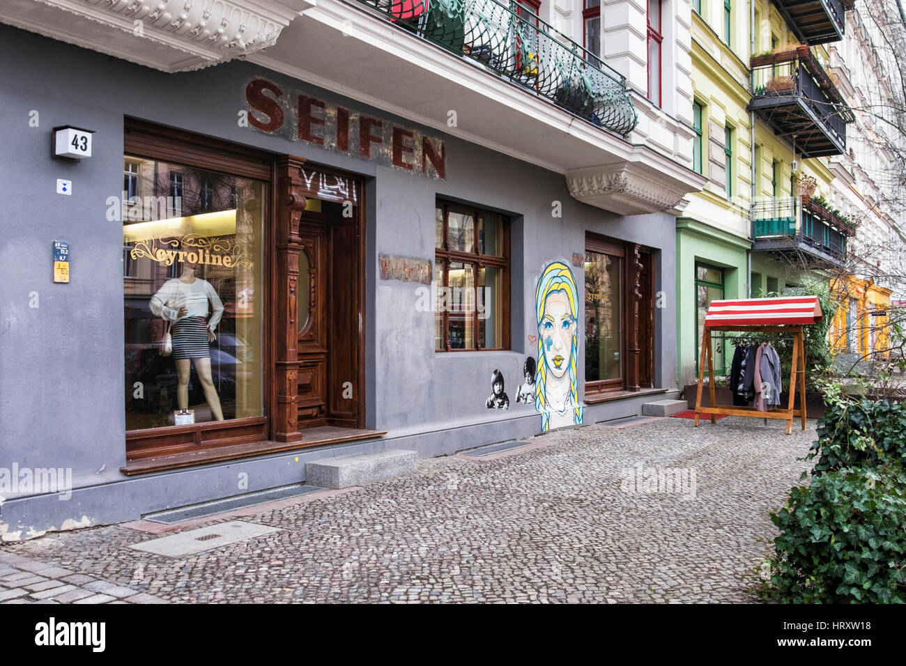Berlin, Prenzlauer Berg. Straßenszene, Cyroline Upmarket Kleidung Shop, alte erhaltene Ladenschild und El Bocho Street art Stockfoto