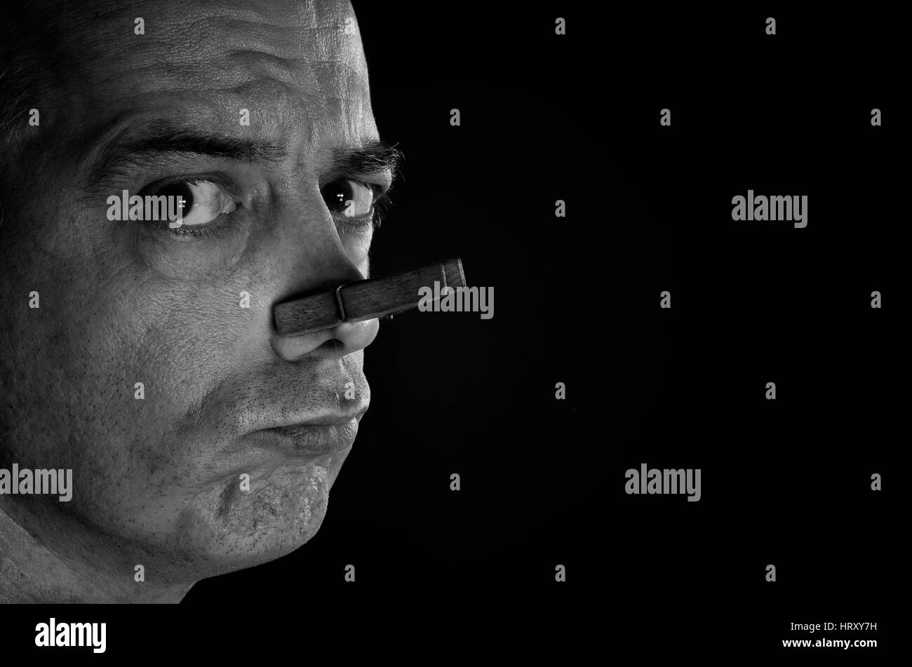 Alte hölzerne Wäscheklammer auf der Nase eines Mannes schützt gegen schlechte Gerüche. Stockfoto